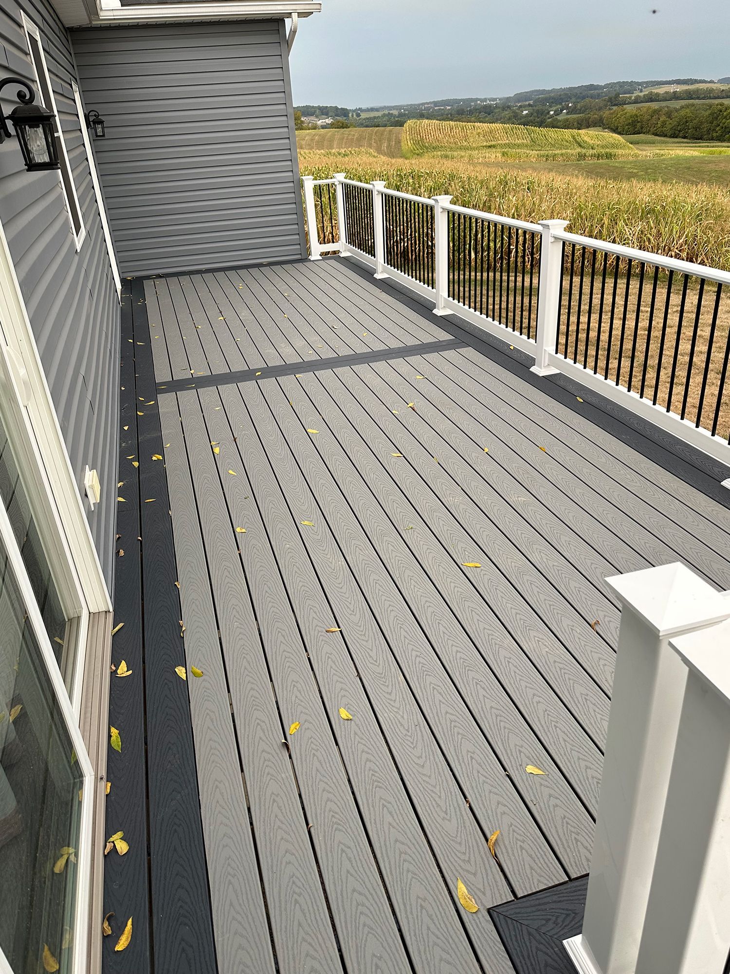 A gray deck with a white railing and a view of a field.