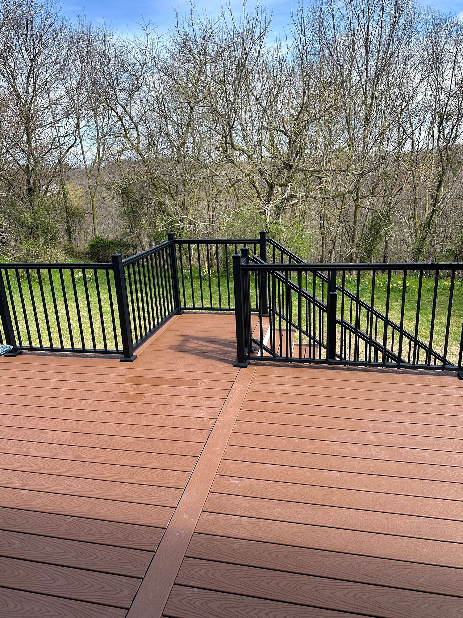 A wooden deck with a black railing and stairs leading up to it.
