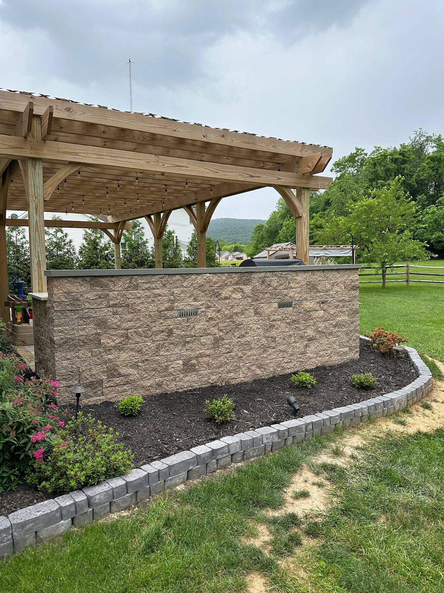 A wooden pergola is sitting in the middle of a lush green field.