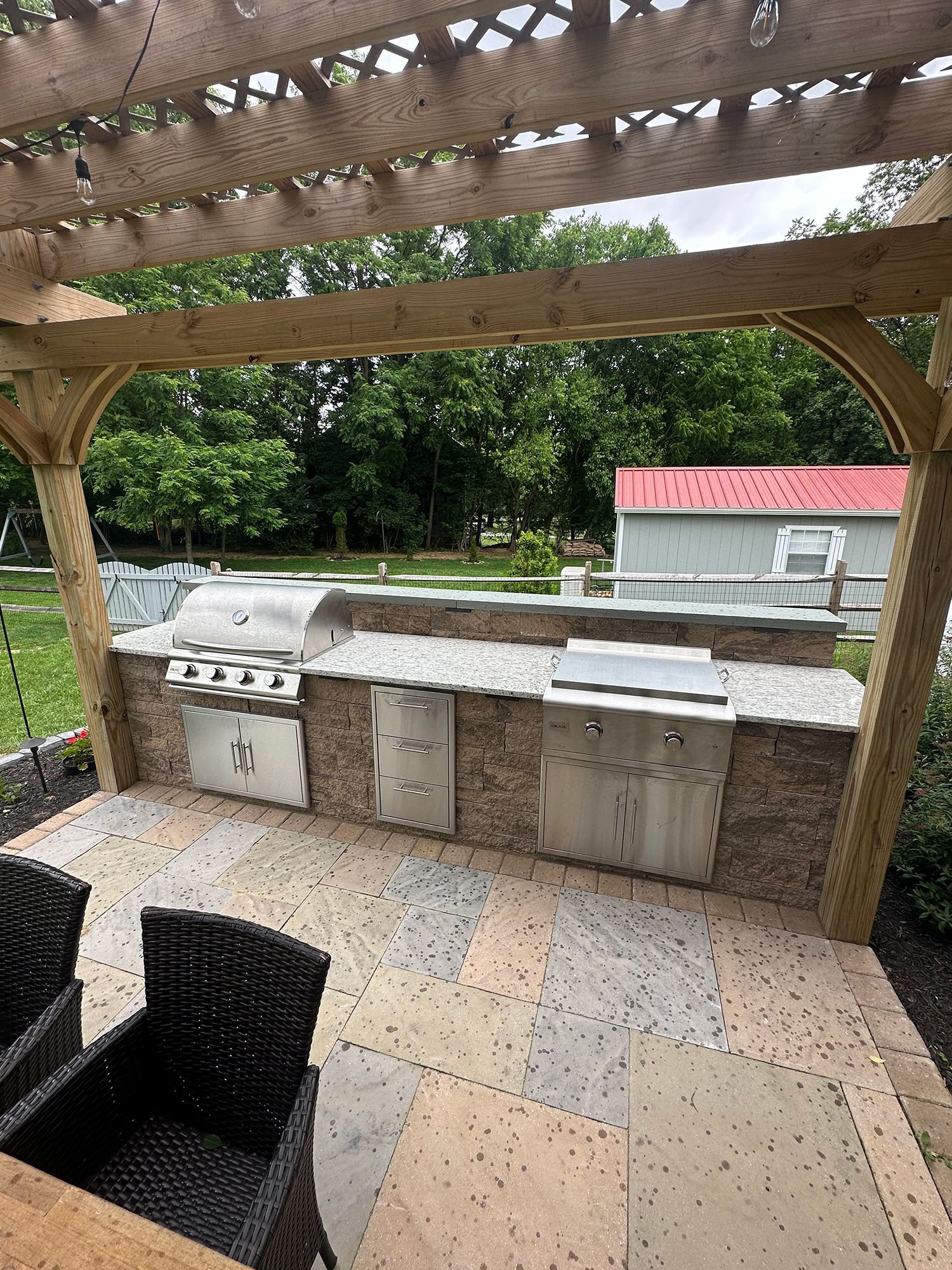 A patio with a grill and chairs under a pergola.