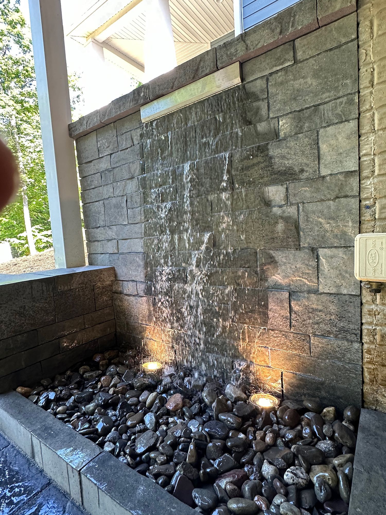 A waterfall is built into a brick wall surrounded by rocks.
