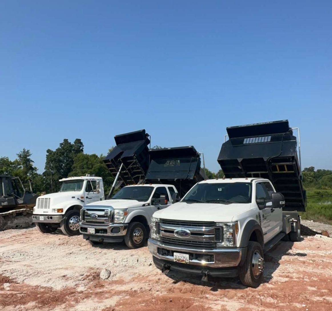 Three dump trucks are parked in a dirt lot