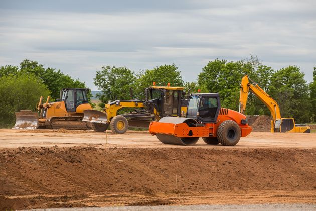 Construction vehicles grading a dirt site under an overcast sky