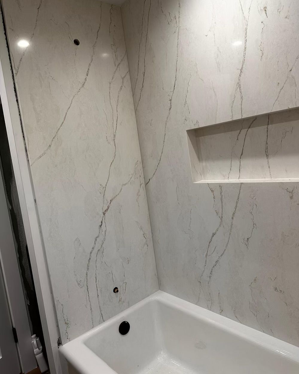 White and beige marble-patterned tiled shower stall with a built-in shelf and a white bathtub.