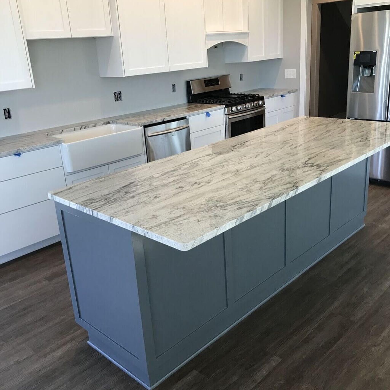 Gray kitchen island with a light-colored granite countertop, white cabinets, and stainless steel appliances.