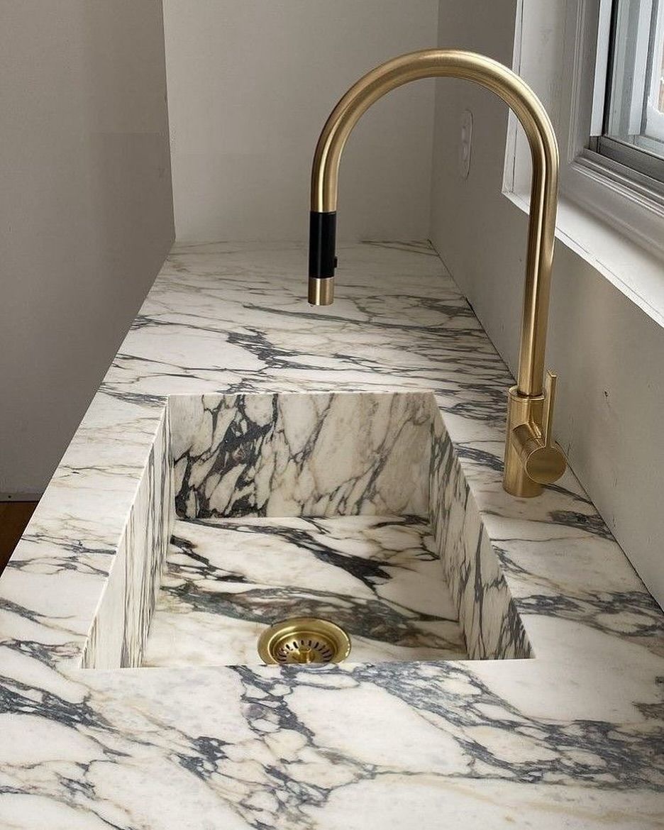 Marble sink with gold faucet. Countertop and sink are white and gray marble.