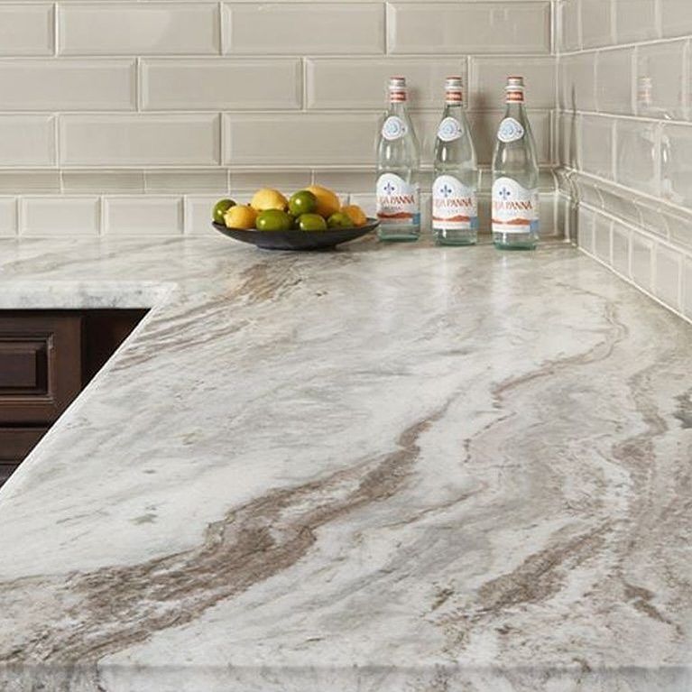 Kitchen counter with marble-like pattern. Bottles and fruit bowl on the surface with tiled backsplash.