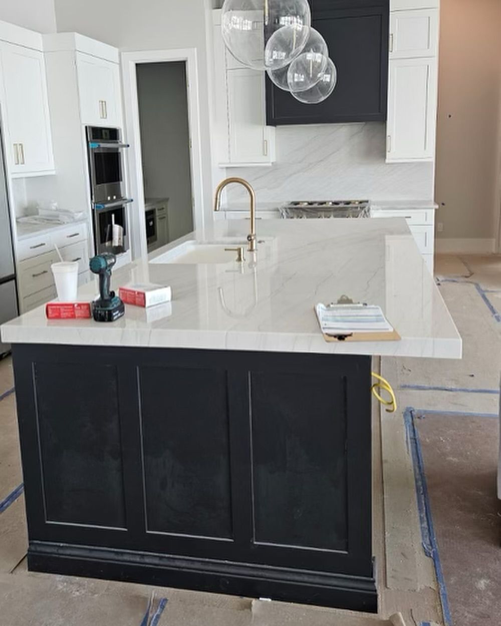 Kitchen island with black cabinets and light countertop, gold faucet, and light fixtures, under construction.