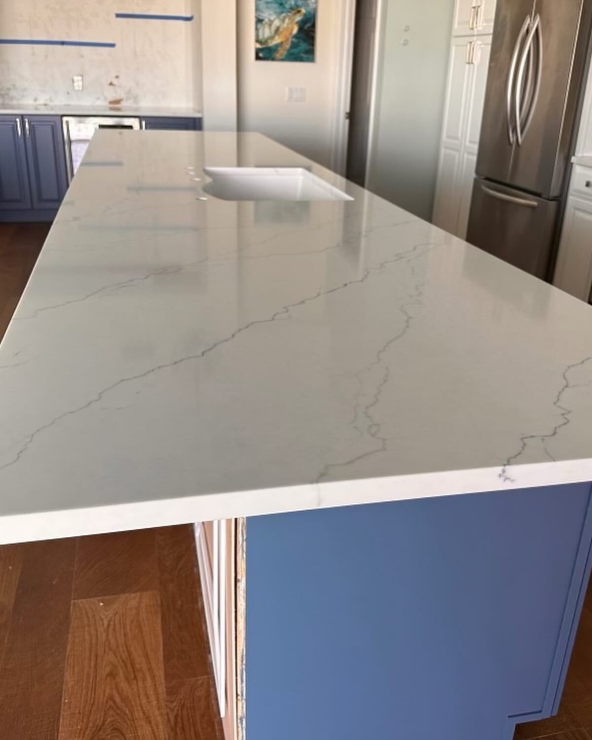 Kitchen island with white countertop, blue cabinets, sink, and stainless steel refrigerator.