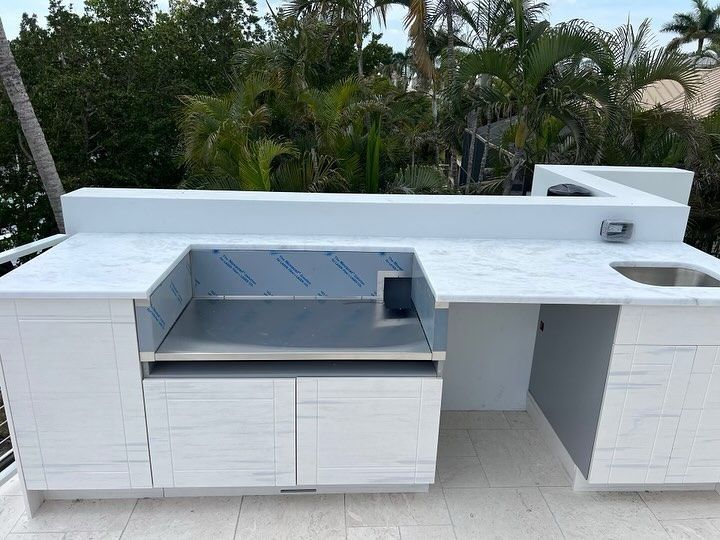 White outdoor kitchen with marble countertop, stainless steel grill, and cabinets.