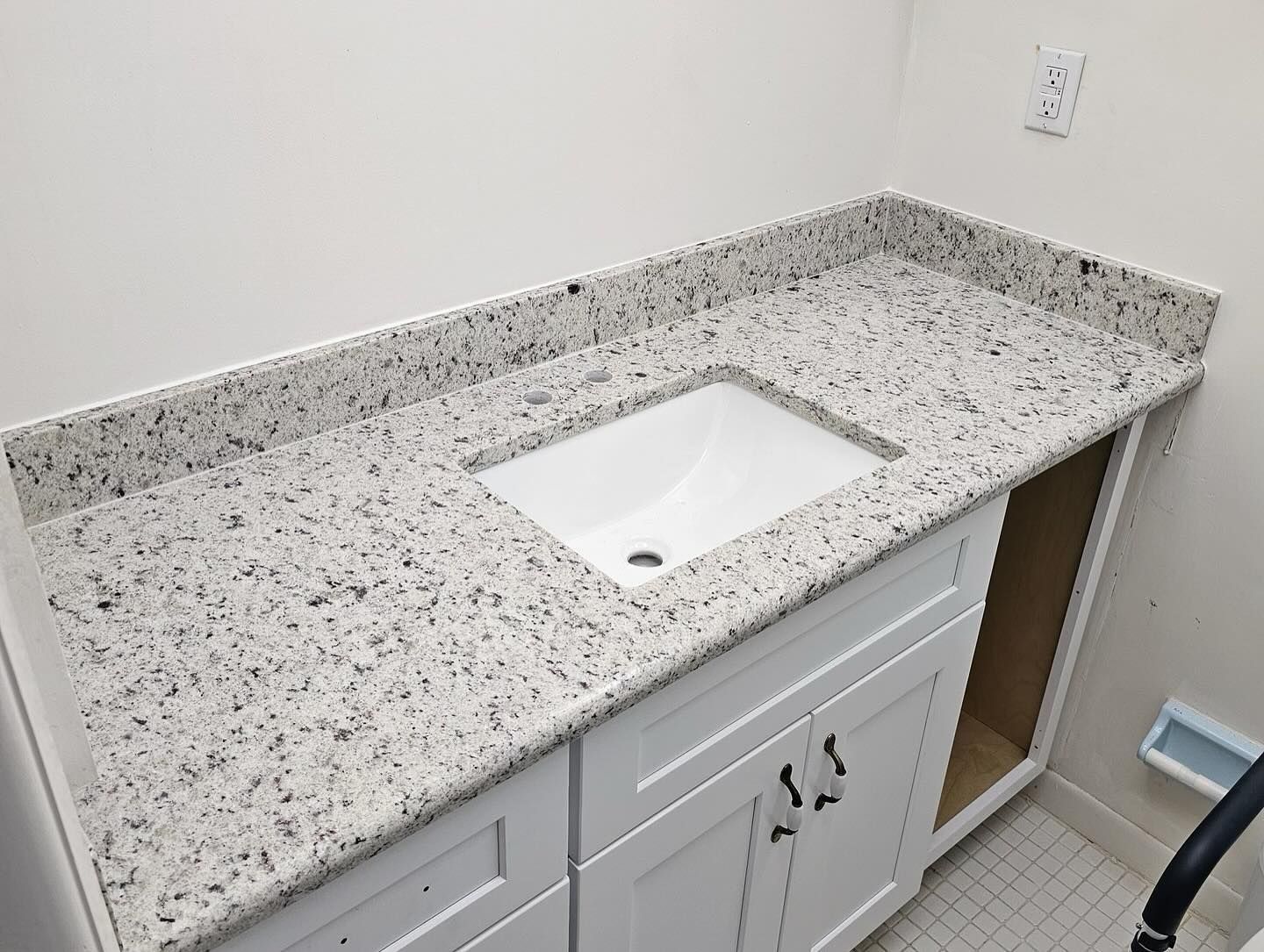 White vanity with a granite countertop and a rectangular sink.