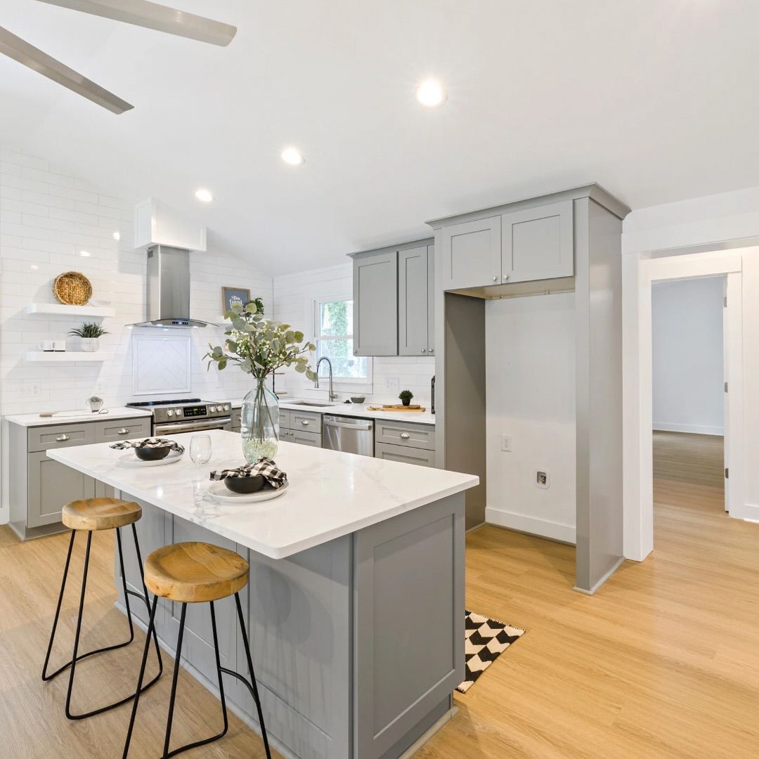 Modern kitchen with gray cabinets, white countertops, and wooden stools at an island.