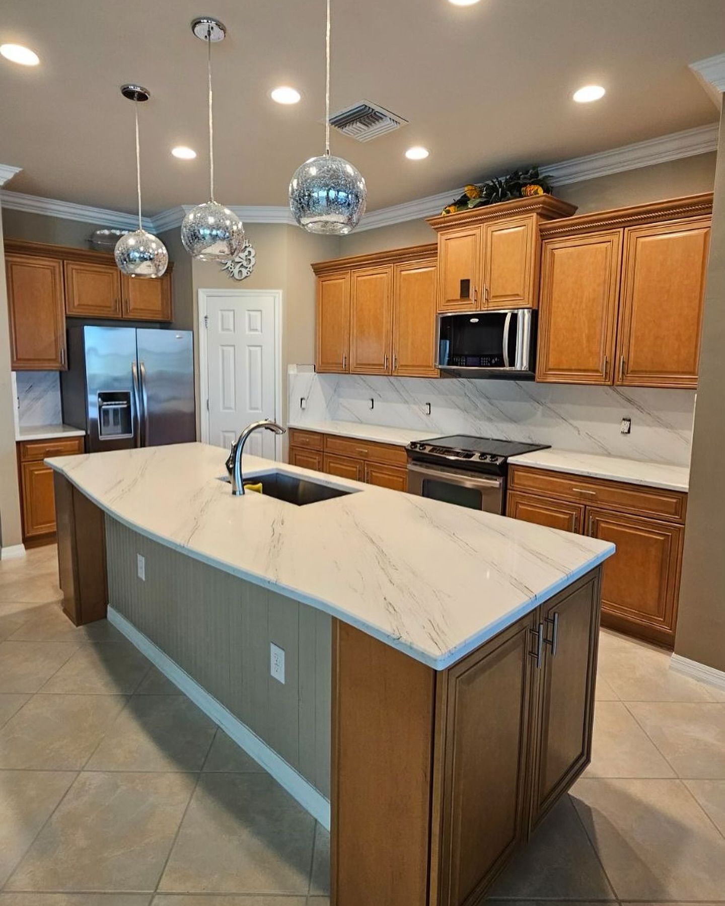 Kitchen with light wood cabinets, white countertops, stainless steel appliances, and a large island.