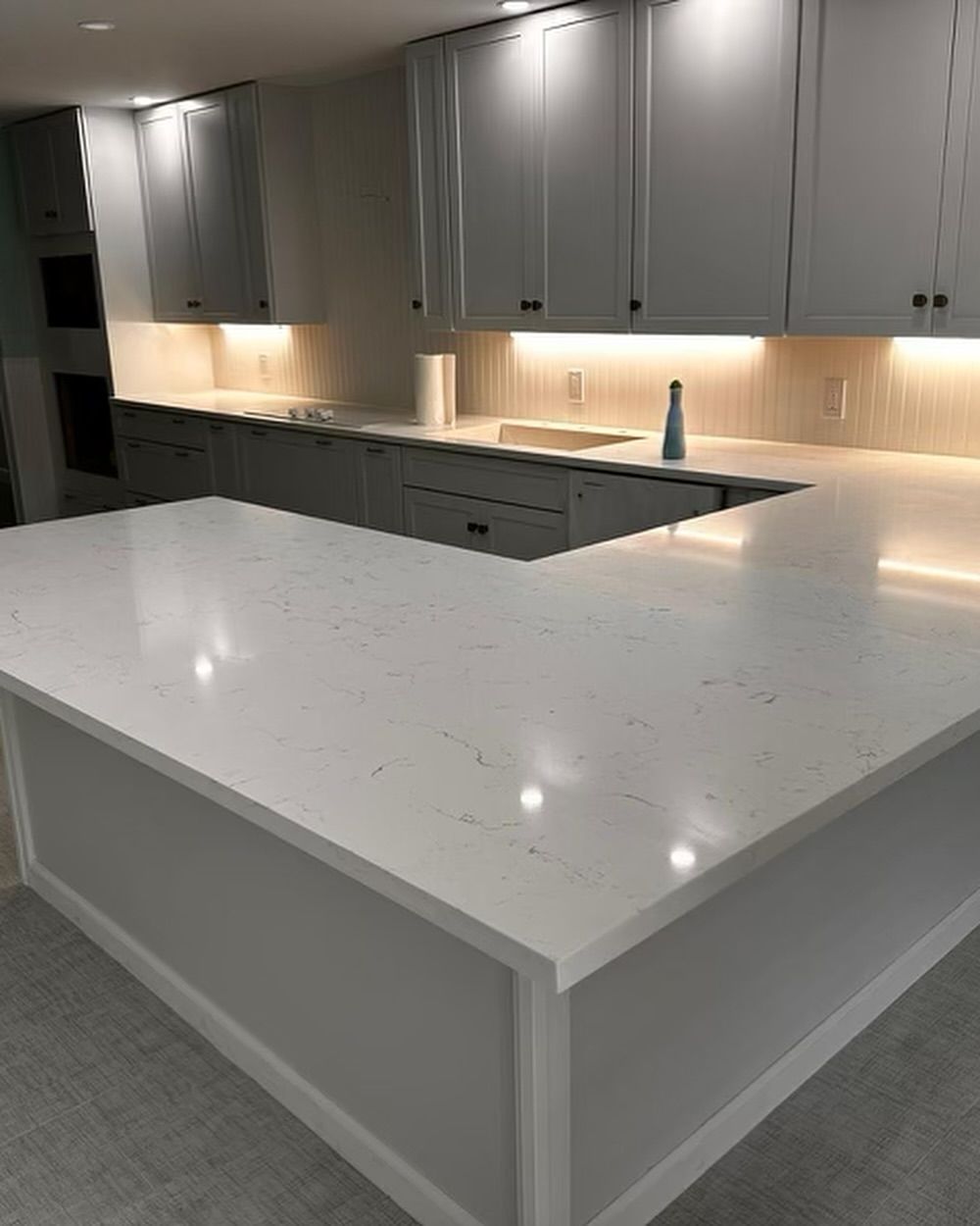 Modern white kitchen with quartz countertops and under-cabinet lighting.