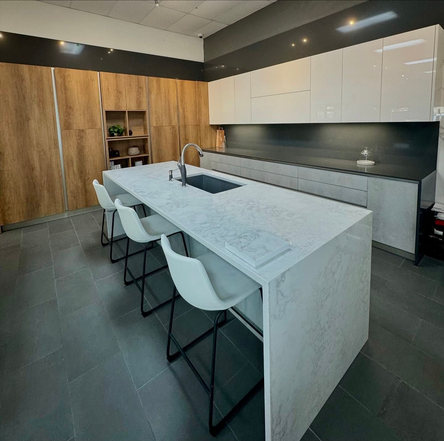 Modern kitchen with white island, seating, wood and white cabinets, and dark countertop.