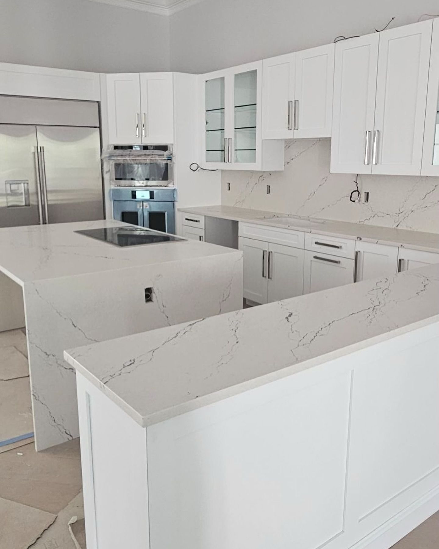White kitchen with quartz countertops and cabinets, built-in appliances, and a central island.