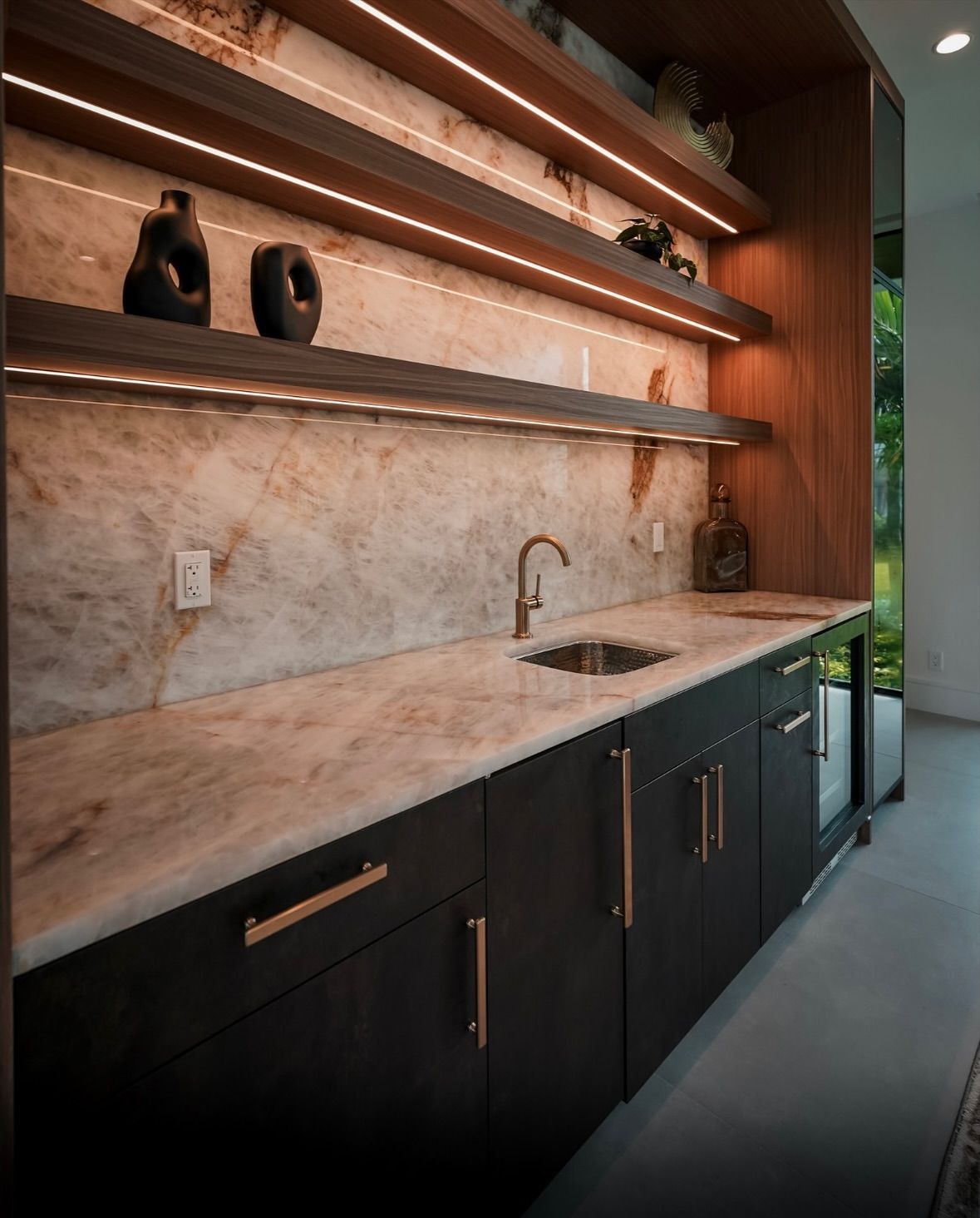 Dark wood bar with marble countertop, cabinets, and open shelves with accent lighting.