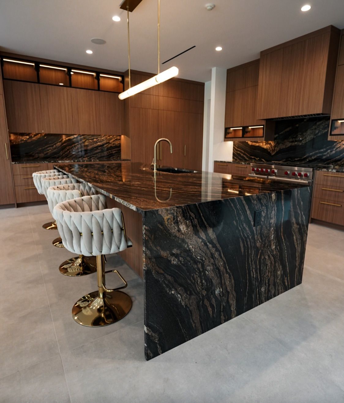 Modern kitchen with large dark granite island, wooden cabinets, and gold accents.