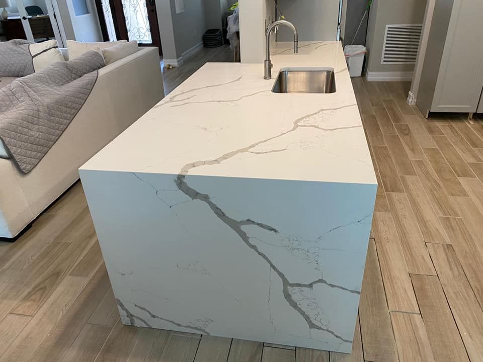 Kitchen island with white countertop featuring gray veining; stainless steel sink and faucet.