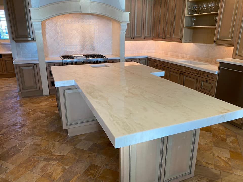 Kitchen with light-colored cabinets, countertops, and a large island. Tiled backsplash and wood flooring.