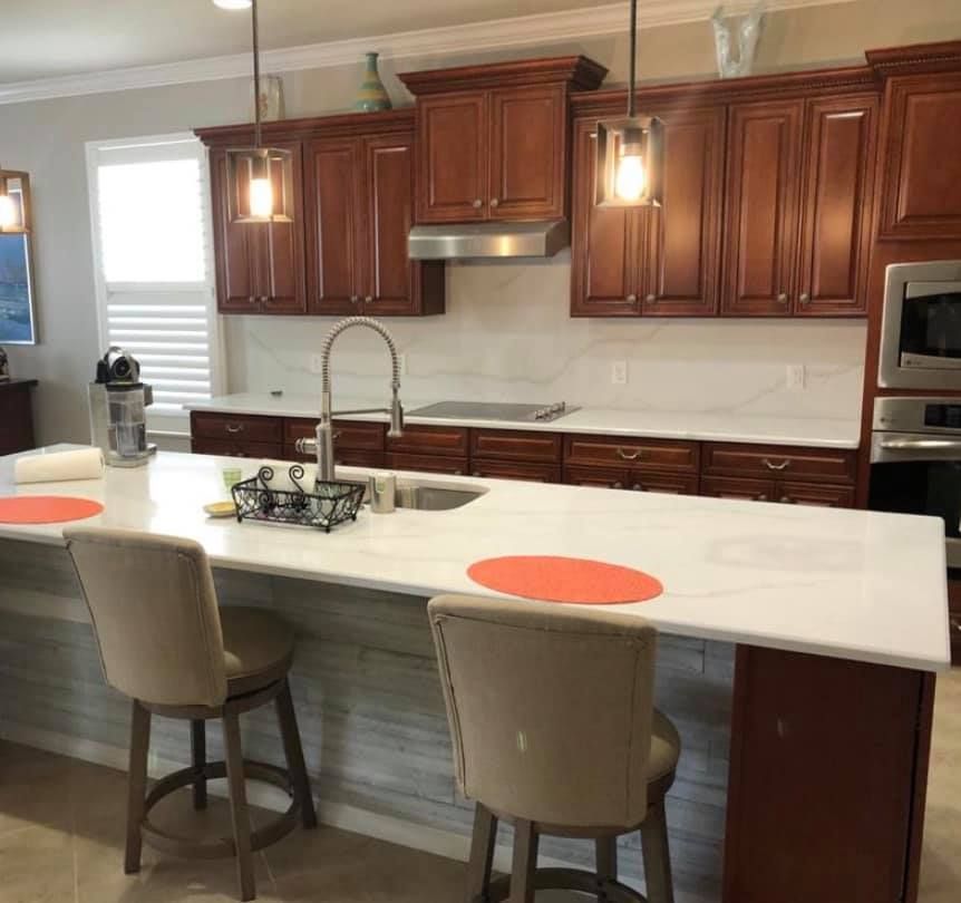 Kitchen with cherry cabinets, white countertops, island with seating, pendant lights, stainless steel appliances.