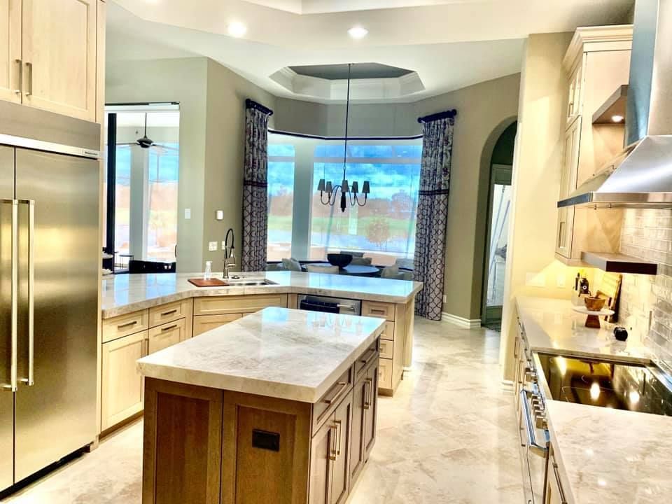 Spacious kitchen with island, stainless steel appliances, and large window overlooking landscape. Beige cabinets and flooring.