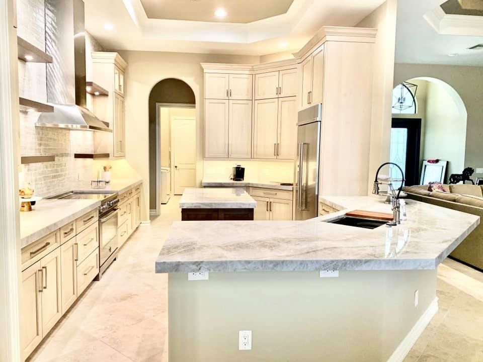 A bright kitchen with light cabinets, stainless steel appliances, and a marble countertop island.