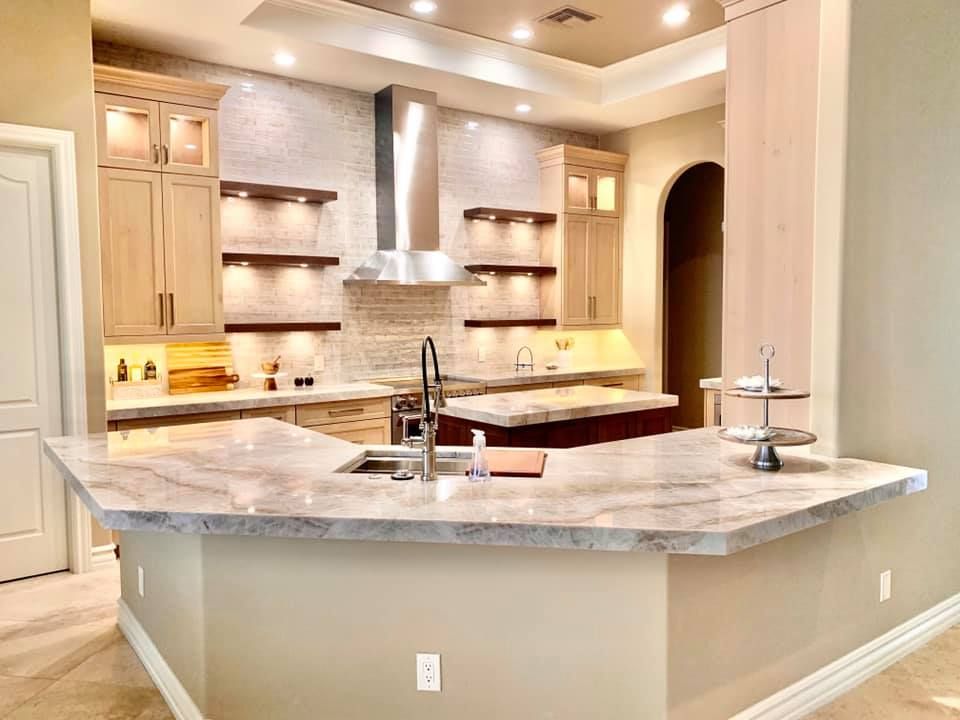 Modern kitchen with light countertops, wood cabinets, and a stainless steel range hood.