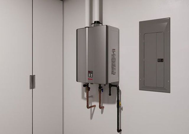 Wall-mounted boiler unit with pipes and an electrical panel on a plain gray utility wall