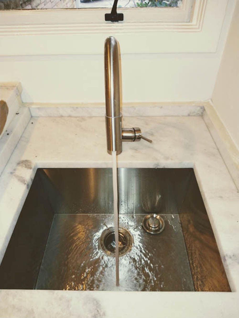 Kitchen sink with running water and a tall chrome faucet over a stainless-steel basin