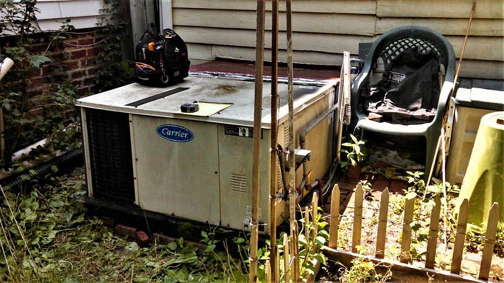 Outdoor air conditioner unit beside a house, with a stroller and garden fence nearby