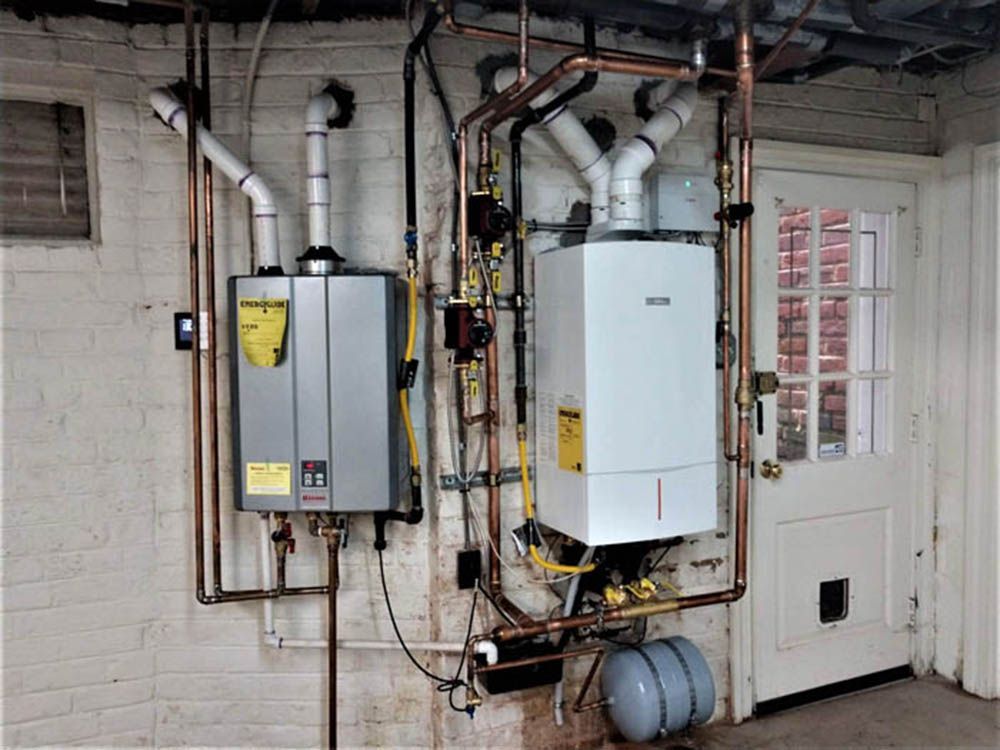 Basement utility room with wall-mounted boilers, pipes, and water heaters beside a door