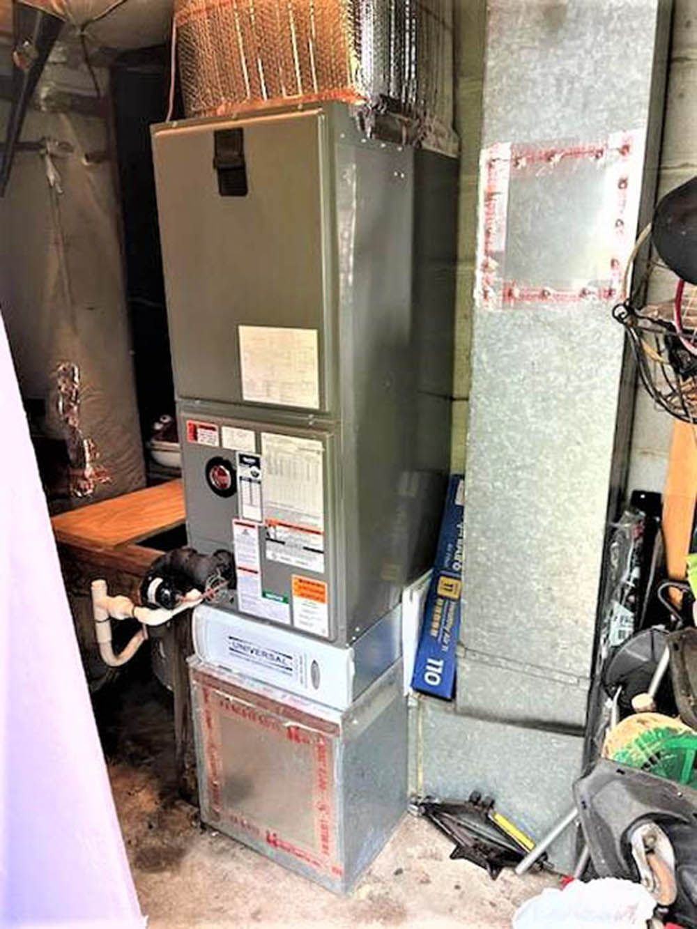 Gas furnace in a utility closet with exposed insulation and ductwork; a cat peeks in at lower left.
