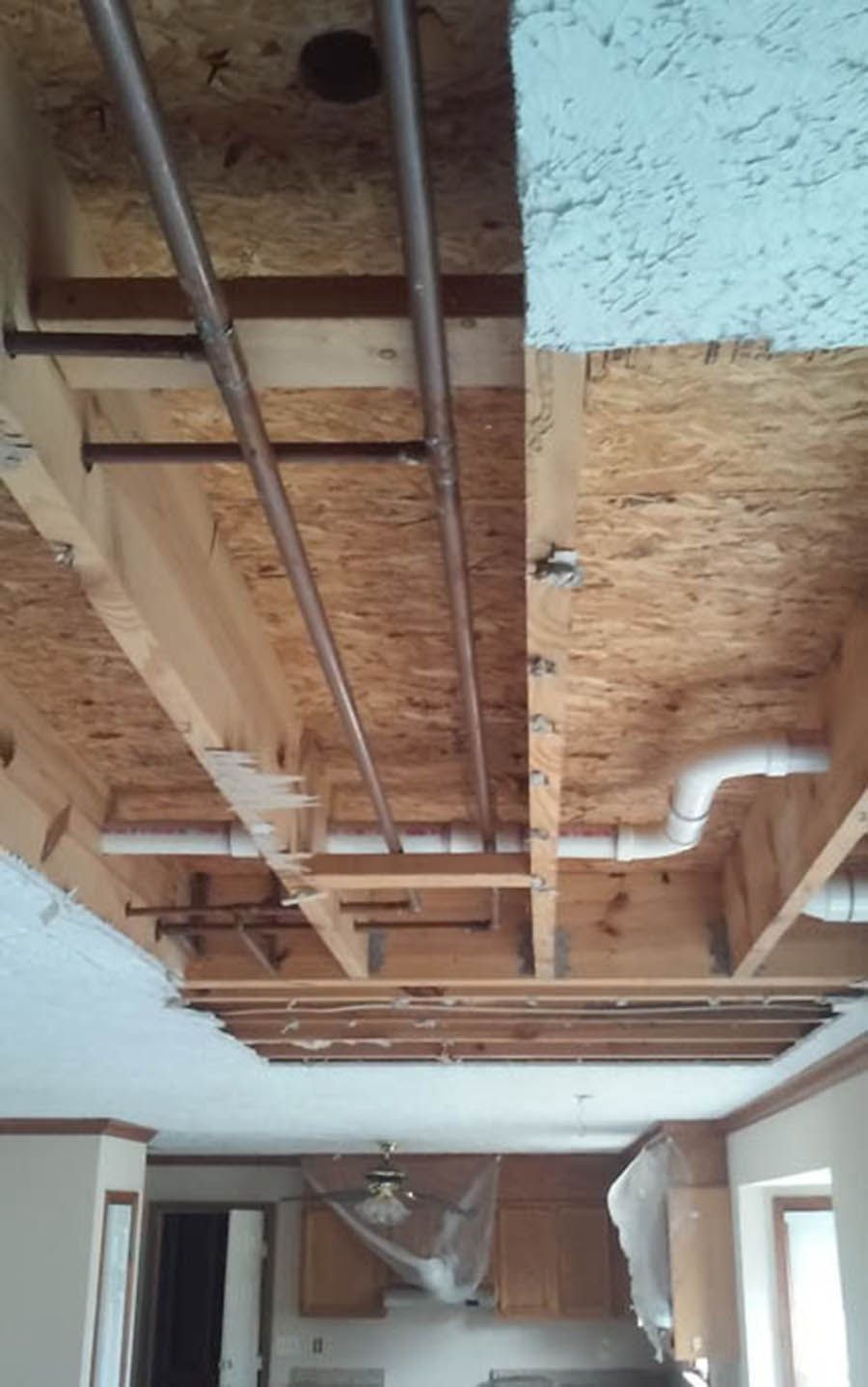 Exposed ceiling framing and ductwork in a room under renovation, with a window and hanging light fixture below.