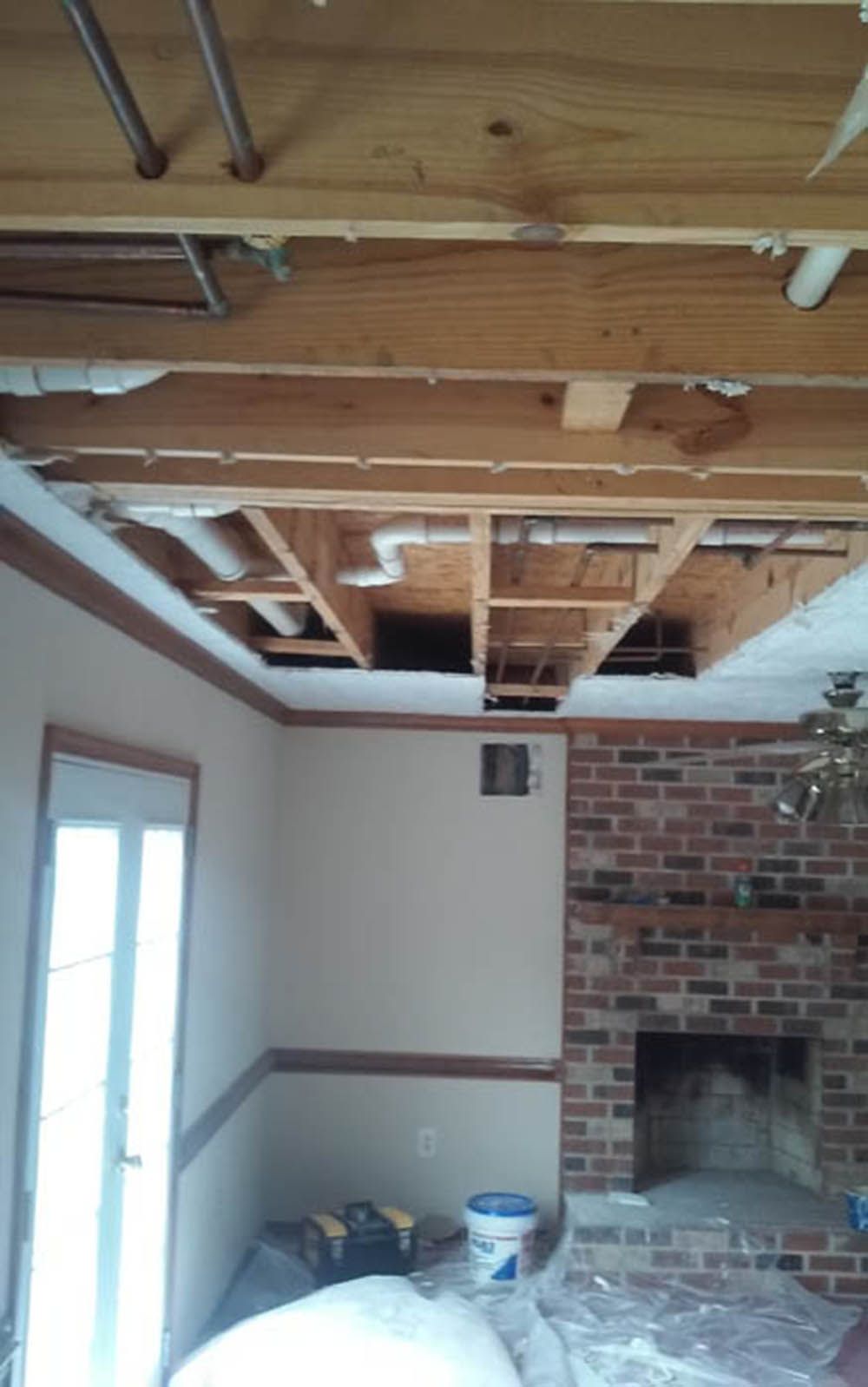 Partially demolished room with exposed wooden ceiling beams, brick fireplace, and debris on the floor