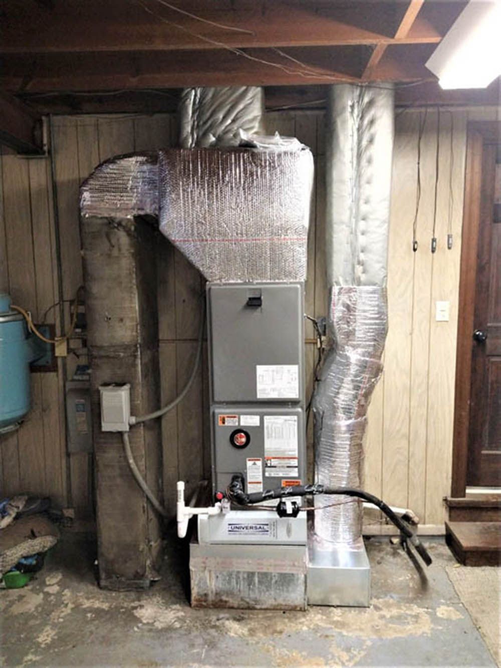 Indoor furnace and HVAC unit with silver ductwork in an unfinished basement utility room.