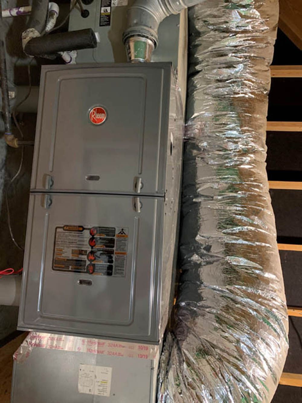 Gray HVAC furnace with attached ductwork in a utility room.