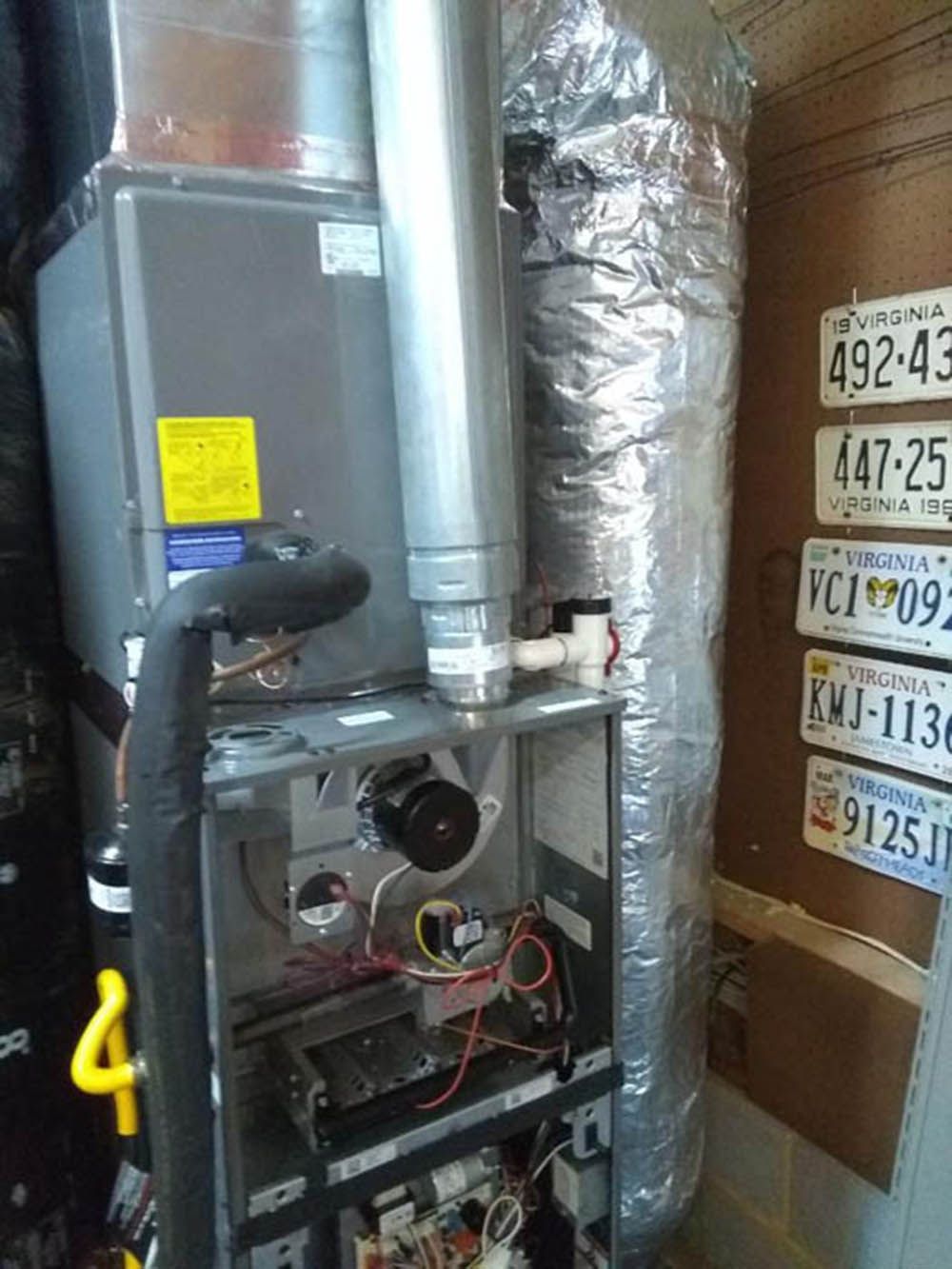 Open furnace and HVAC ducts in a utility closet with license plates mounted on the wall
