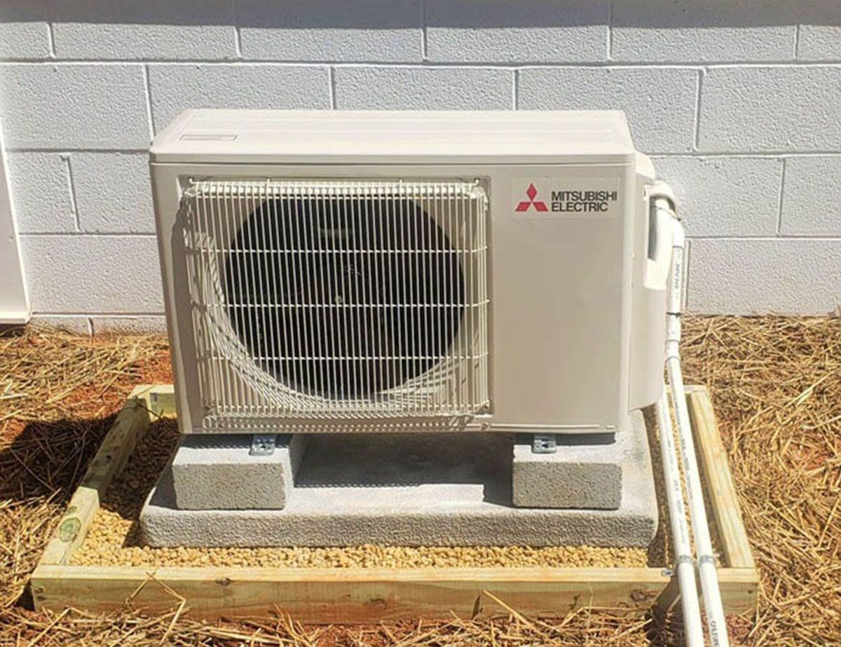 Outdoor Mitsubishi air conditioner unit on a concrete pad beside a building wall