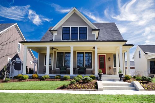 Front view of a yellow house with a white porch, black shutters, and a red front door under a blue sky