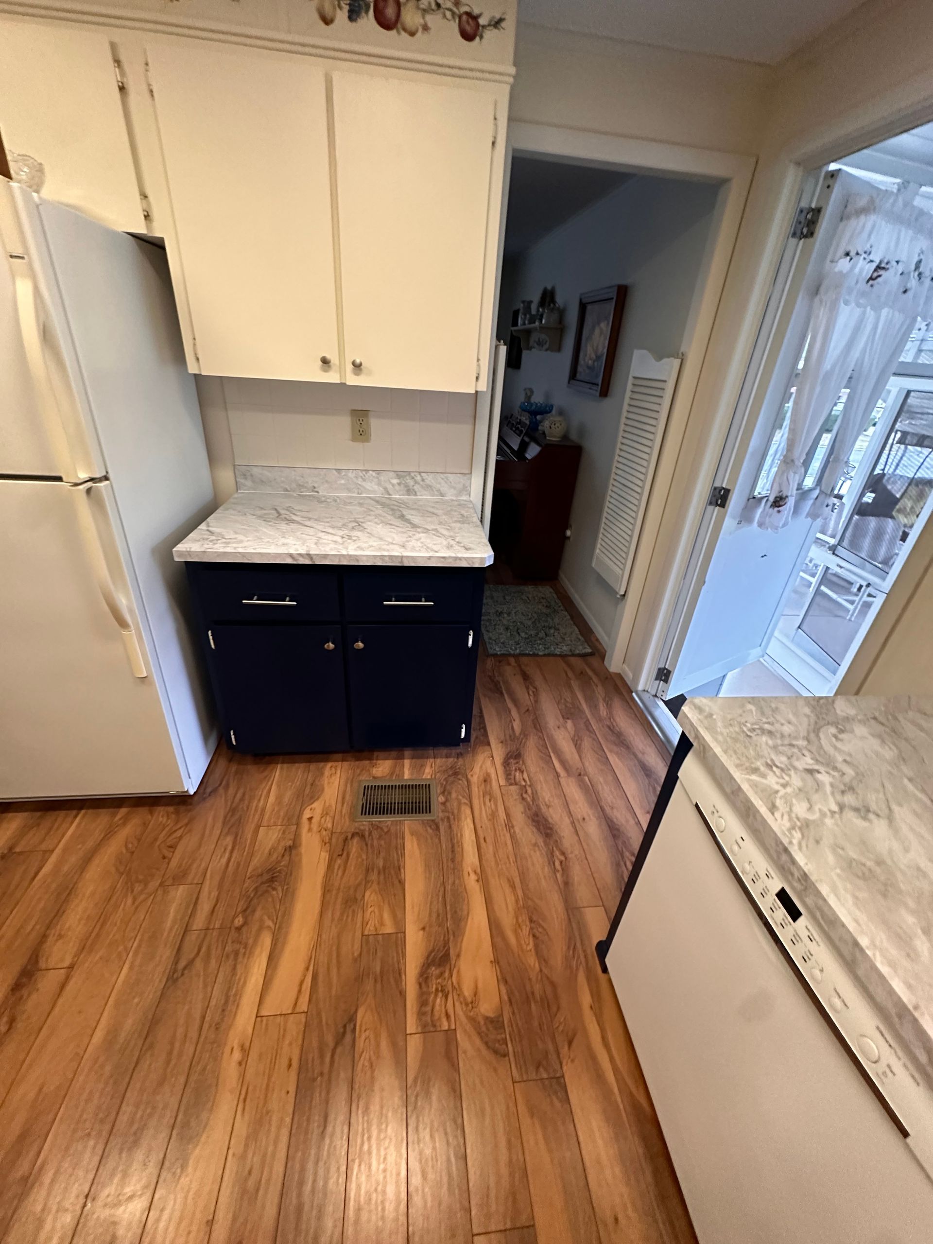 A kitchen with hardwood floors, white cabinets, and a refrigerator