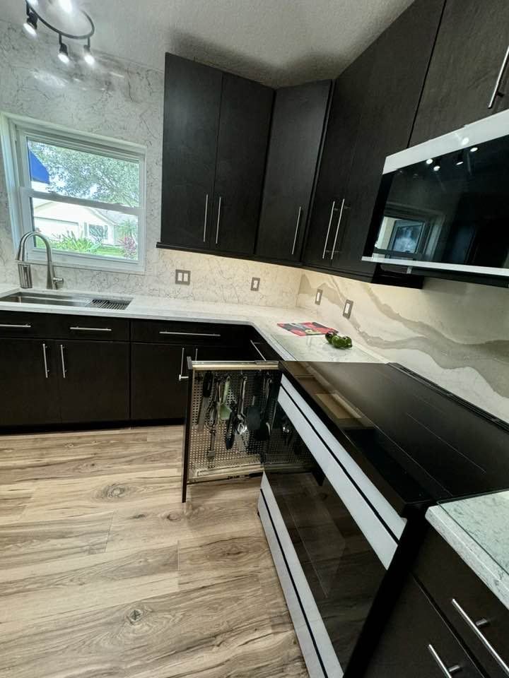 A kitchen with black cabinets, a black stove top oven, a sink, and a window