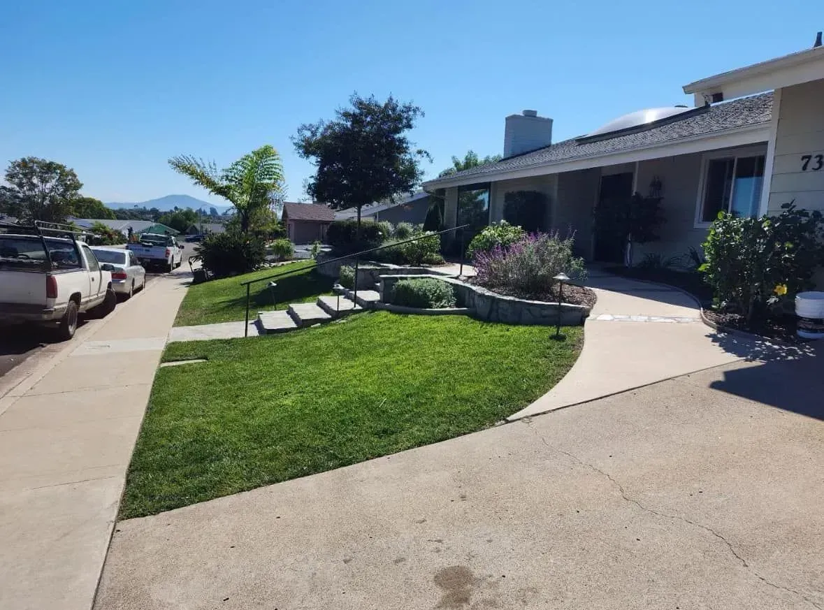 Front yard with green lawn, stone steps, and a curving concrete walkway leading to a house with a gray roof.