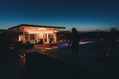 A woman is standing in front of a house with a pool at night.