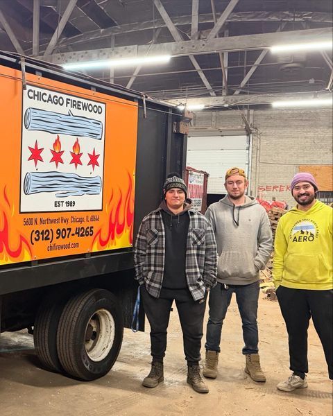 Three men pose by a Chicago Firewood truck. They stand in a garage setting.