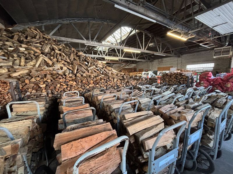 Stacks of firewood, neatly arranged on carts, inside a warehouse.