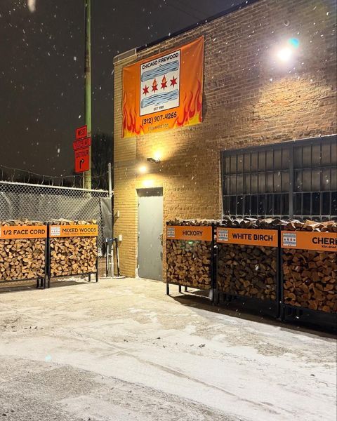 Snowy outdoor scene with firewood racks, Chicago flag banner, and brick building.