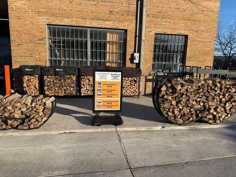 Wood for sale outside a brick building. Bundles of firewood and a sign with pricing.