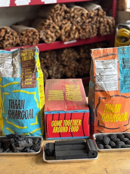 Bags and box of Thaan Charcoal with samples, in front of shelves of wood.