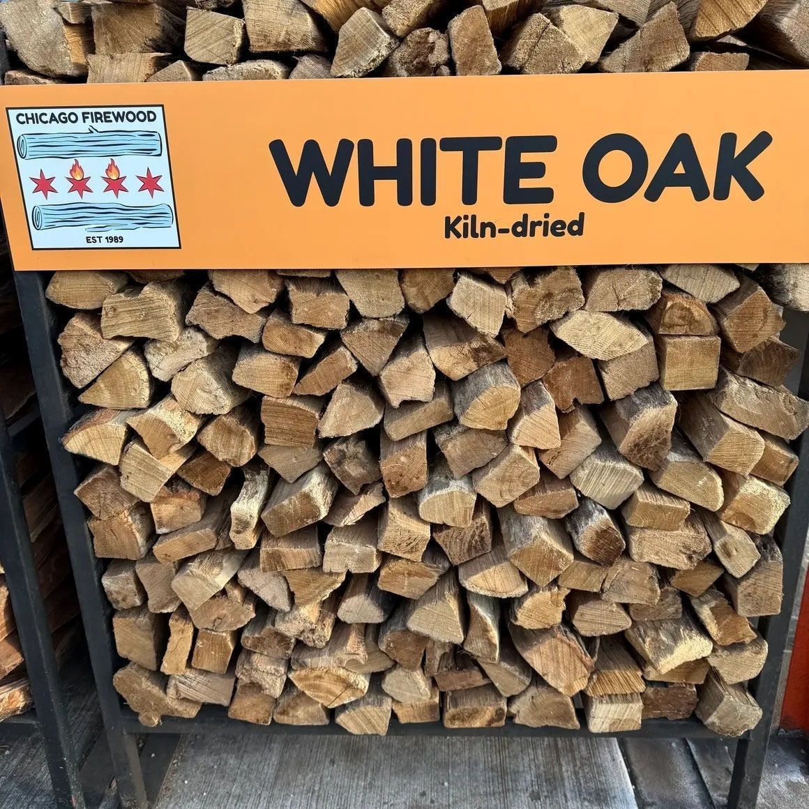 White oak kiln-dried firewood stacked in a metal rack with sign: White Oak, Chicago Firewood.